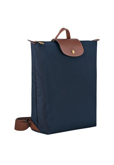 Navy blue nylon backpack with a brown leather flap and handle, gold hardware, and adjustable brown strap. Features a front pocket detail.