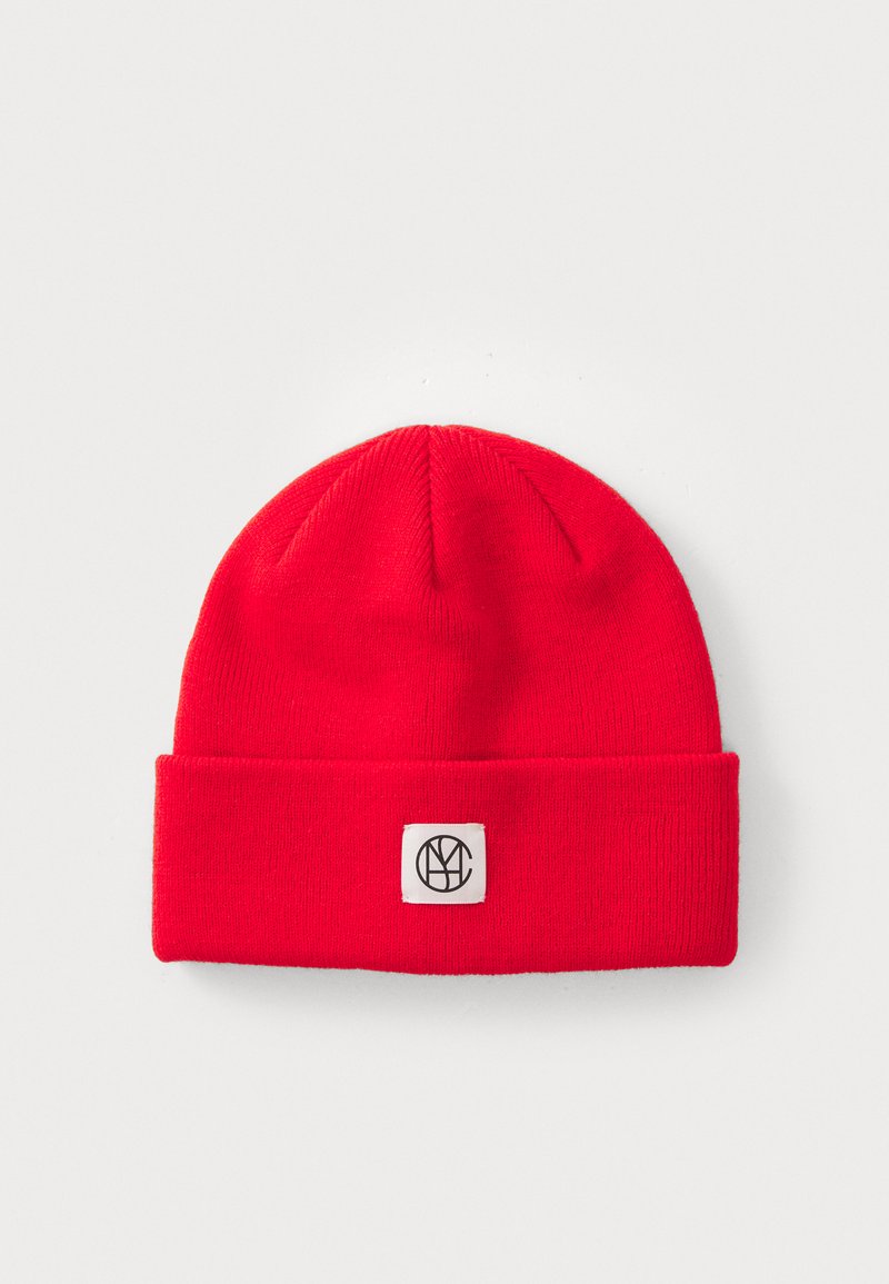 Red knit beanie with a folded cuff and a square logo patch featuring black letters on a white background. Textured fabric.