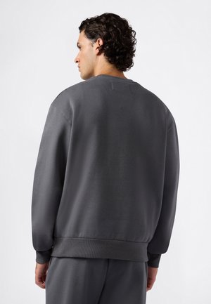 Sudadera gris con un escote redondo y dobladillo acanalado. Confeccionada en un material suave, presenta un ajuste relajado y un diseño minimalista.