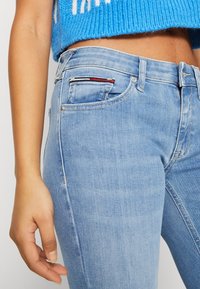 Světle modré džíny s úzkým střihem, s jemnými vyblednutími, vysokým pasem a malou kapsou s červenými, bílými a modrými akcenty.