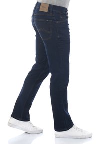 Jeans de mezclilla azul oscuro con corte recto, diseño de cinco bolsillos y costuras en contraste. Presentan una etiqueta de cuero en la cintura.