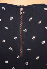 Tessuto nero aderente con piccoli motivi floreali bianchi, con una zip di rame visibile sul retro.