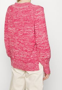 Roze gebreide trui met een textuur en gemarmerd patroon. Heeft een ronde halslijn en losse, geplooide mouwen. Zijsplitten aan de zoom.
