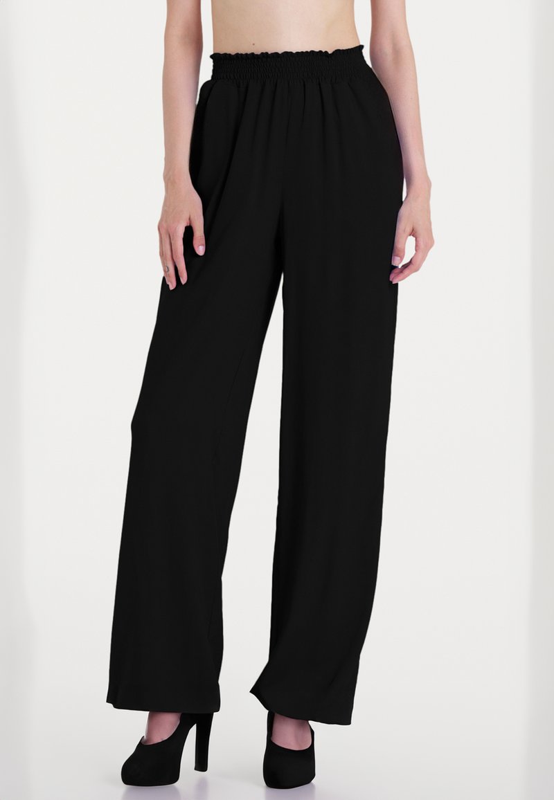 Pantaloni neri a gamba larga con vita a balze, realizzati in un tessuto leggero e caratterizzati da una silhouette fluida, abbinati a tacchi alti neri.