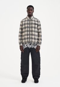 Plaid zip-up shirt in cream and black over a black graphic t-shirt; paired with distressed black jeans and black shoes.