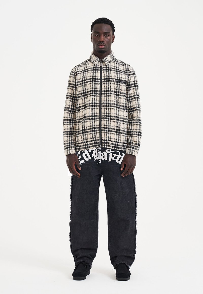 Plaid zip-up shirt in cream and black over a black graphic t-shirt; paired with distressed black jeans and black shoes.