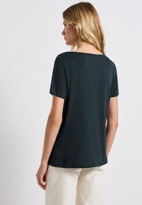 T-shirt vert foncé à manches courtes avec un col rond et une coupe décontractée, fabriqué à partir d'un matériau doux, dos partiellement visible.