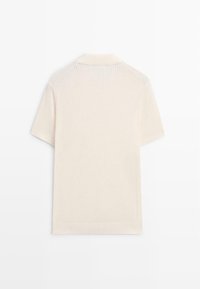 Polo a maniche corte color crema con collo, a coste, mostrata piatta da dietro su sfondo bianco.