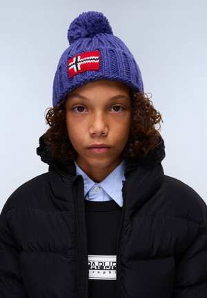 Bonnet en tricot violet avec un pompon bleu et un patch du drapeau norvégien. Porté avec une veste matelassée noire, un sweat-shirt gris et une chemise à col blue.