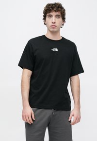 Μαύρο βαμβακερό μπλουζάκι με κοντά μανίκια, στρογγυλή λαιμόκοψη και λευκό λογότυπο στο αριστερό στήθος. Συνδυάζεται με γκρι φόρμα.