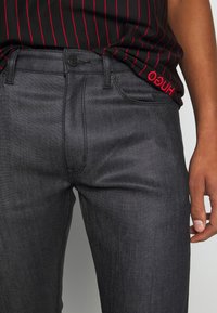 Svarta denimjeans med en figurnära design, texturerat tyg och subtil lyster. Har en knappstängning och sidofickor.