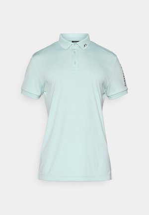 Light blue polo shirt made of soft fabric, featuring a collar, three buttons, and branded accents on the sleeve. Short sleeves.