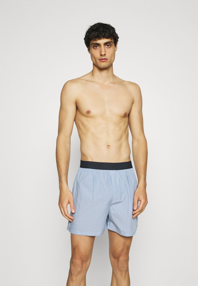 Boxer (slip) a righe blu e bianche realizzato in tessuto leggero, con una cintura elastica nera e una vestibilità ampia.