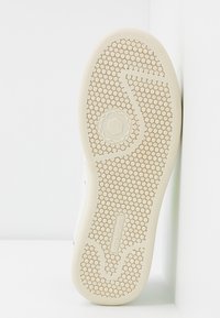 Podeszwa buta z heksagonalnym wzorem i wytłoczonym napisem "Master of Arts", umiejscowiona pionowo na białym tle.