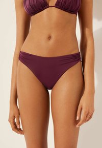 Bikiniunterteil in tiefem Burgunderrot, mit gerafften Seitendetails und glatter Oberfläche. Entworfen für eine figurbetonte Silhouette und Komfort.