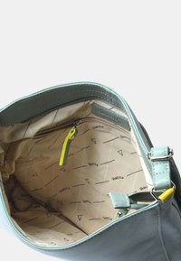 Ljusgrön läderhandväska med dragkedjestängning, med en beige inredning med geometriska mönster och en gul dragkedja för fickan.