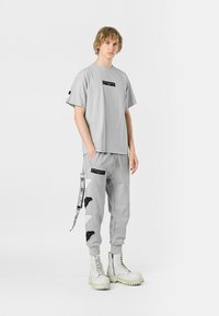 Camiseta gris de manga corta y joggers a juego con acentos gráficos negros, combinados con botas de combate blancas. Tejido suave; ajuste relajado.