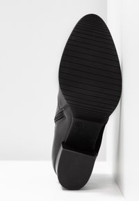 Bottine en cuir noir avec un talon bloc bas, montrant la semelle avec des rainures horizontales et le numéro de taille 37 embossé.