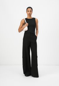 Zwarte mouwloze top van textuurstof, wijde zwarte broek met zijzakken en een kleine lichtroze crossbody tas.