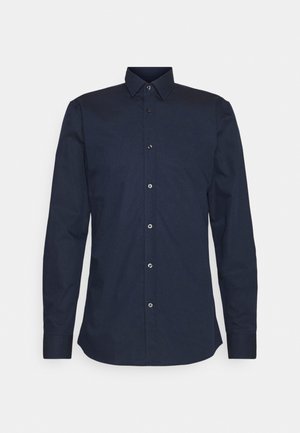 Chemise bleu marine à manches longues avec col classique, boutons sur le devant et silhouette cintrée sur un fond uni.