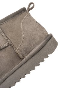 Grå ruskind ankellærred med trækflig, synlige syninger og tyk tekstureret sål med dybe slidbaner, vist i nærbillede.