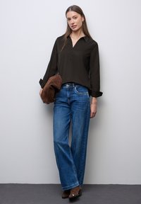 Camisa de botones negra con cuello, vaqueros de pierna ancha azules, clutch de ante marrón y botas de tobillo marrones sobre un fondo neutro. Textura suave.