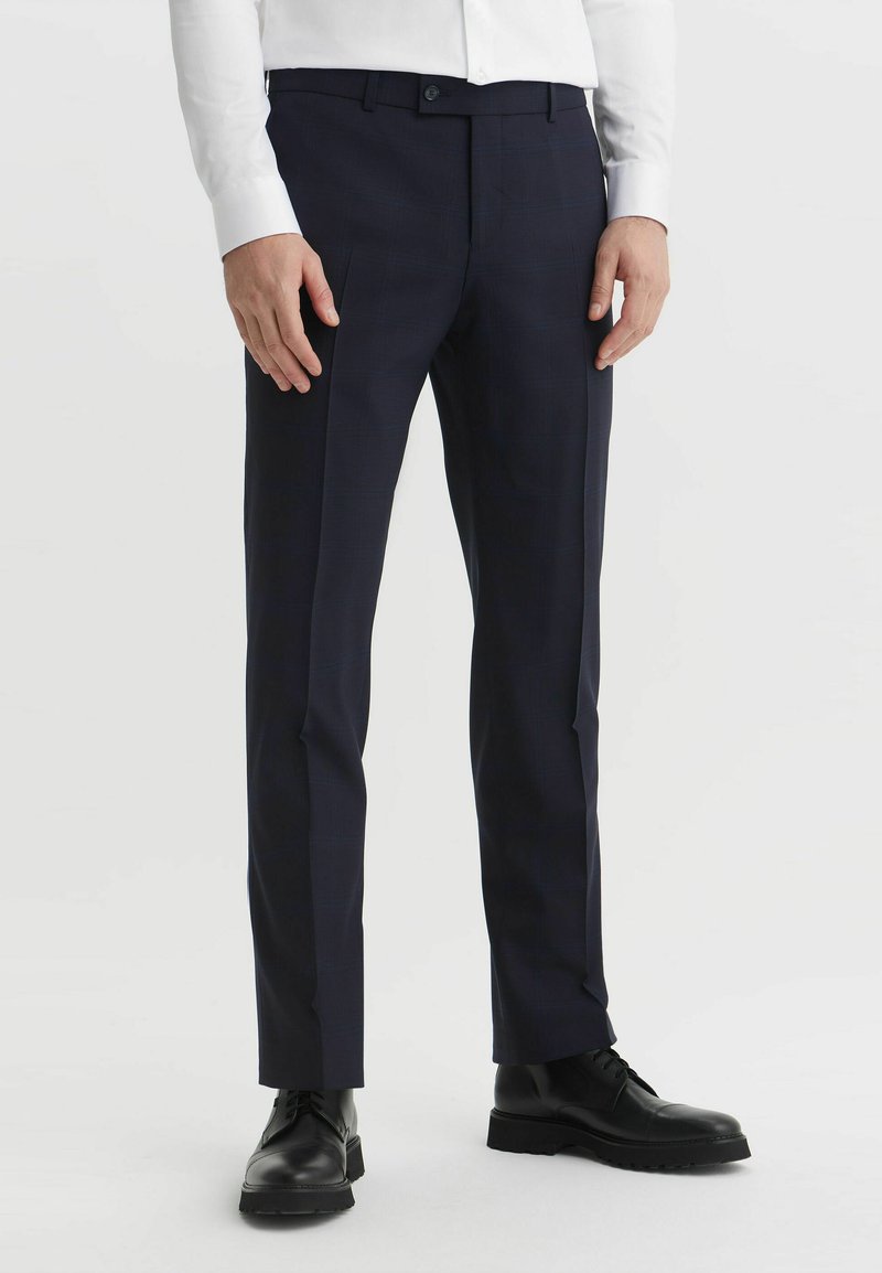 Granatowe, dopasowane spodnie w kratę, wykonane z gładkiego materiału, z płaskim przodem i slim fit, w zestawieniu z czarnymi butami na sznurówki.