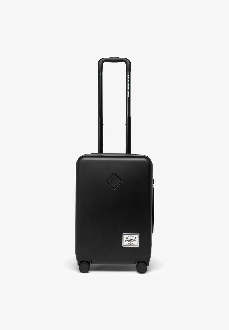 Valise rigide noire avec un logo en forme de diamant, deux roues en caoutchouc, une poignée extensible et une petite poche avant avec une étiquette.