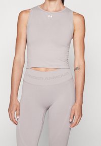 Ljusgrå ärmlös atletisk crop top med rund halsringning, sömlös design och Under Armour-logotyp på bröstet, tillsammans med matchande leggings.