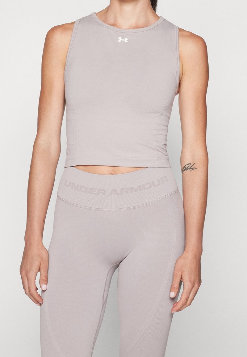 Ljusgrå ärmlös atletisk crop top med rund halsringning, sömlös design och Under Armour-logotyp på bröstet, tillsammans med matchande leggings.