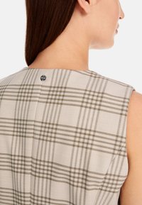 Ärmellose Bluse in hellbeige mit einem Karo-Muster in olivgrün. Verfügt über einen Knopfverschluss am Rücken. Glatte Textur.