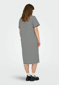 Proužkované černobílé bavlněné šaty s krátkými rukávy, střední délkou, volným střihem a bočními rozparky na lemu. Nošeno s černými botami.
