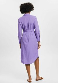 Lila långärmad skjortklänning med bälte i midjan, rund nederkant och mjukt tyg. Inkluderar knappryggar på ärmarna och krage.