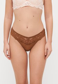 Hnědé krajkové tanga s květinovým vzorem na pase, s hladkým, průhledným tělem a malým detailem uprostřed.