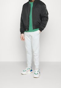 Black bomber jacket, green shirt, gray sweatpants, white sneakers with colorful accents. Jacket features ribbed cuffs and a front zipper.
