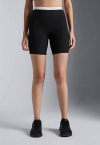 Shorts de sport noir à côtes avec une large ceinture blanche, design ajusté et texture lisse, portés avec des baskets noires.