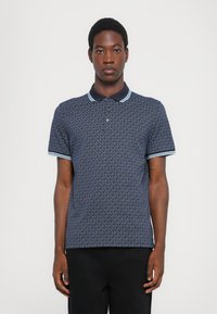 Πολυεστερικό μπλε πόλο μπλουζάκι με μοτίβο λογότυπου σε όλη την επιφάνεια, ριγωτό γιακά με ανοιχτό μπλε λεπτομέρειες και κοντά μανίκια με ταιριαστά μανίκια.