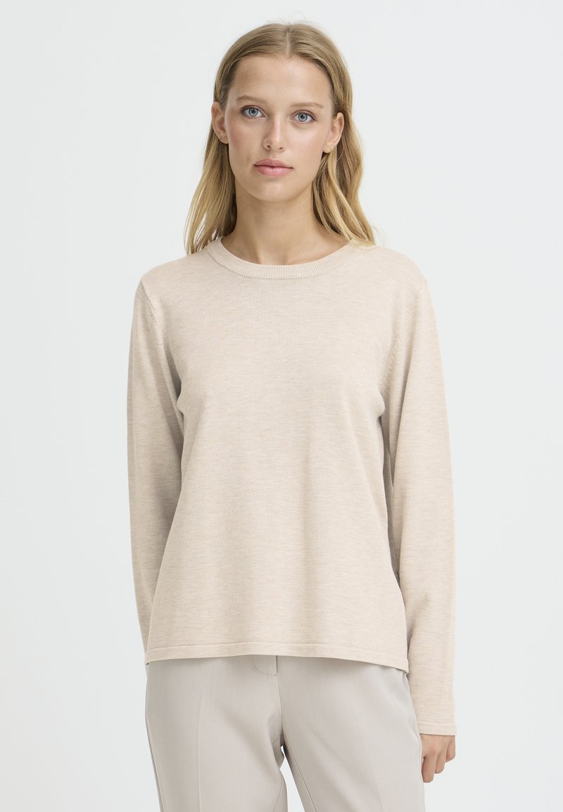 Beiger Pullover mit langen Ärmeln, Rundhalsausschnitt, weiche Textur, lockere Passform, leicht abgerundeter Saum, kombiniert mit hellen Hosen.