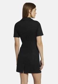 Schwarzes Kurzarmkleid mit strukturiertem Kragen, taillierter Passform, seitlichen Taschen und einem Schlitzausschnitt auf der Rückseite für Bewegungsfreiheit.