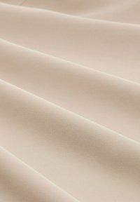 Tissu beige avec une surface lisse et texturée, présentant des ondulations subtiles et une couleur claire uniforme.