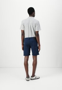 Chemise à manches courtes rayée en gris clair et blanc, associée à un short bleu foncé. Le modèle porte des baskets claires avec des accents noirs.