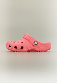 Sabot rose à enfiler avec des trous de ventilation et une bride de talon réglable comportant un badge circulaire avec logo sur un fond neutre.