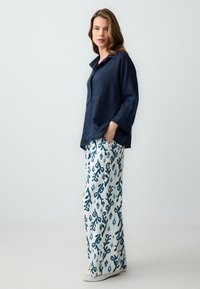 Chemise en lin bleu marine avec col, associée à un pantalon blanc à motif floral bleu. Les deux pièces ont une coupe décontractée et une texture respirante.