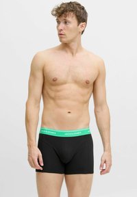 Melni kokvilnas boksa šorti ar zaļu elastīgu jostasvietu, uz kuras ir balti uzraksts "JACK & JONES". Gluda tekstūra un pieguloša forma.