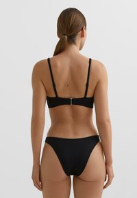 Črni bikini zgornji del z nastavljivimi naramnicami in pravokotnim kovinskim zaponkom na hrbtni strani, združen z ujemajočimi nizko prirezani bikini spodnjicami. Rebrasta tekstura.