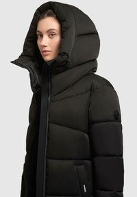 Sort puffjakke med en stor, rund hætte, der har en frontlynlås, sidelommer og en glat, struktureret overflade.
