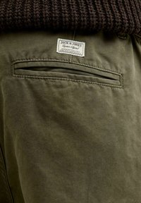 Pantaloni verde oliva con una texture liscia, una tasca posteriore con apertura inclinata e un'etichetta di stoffa con la scritta "JACK & JONES."