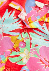 Kleurig overhemd met korte mouwen, versierd met een bloemenprint in roze, groen en blauw, met rode knopen en een kraag die wordt benadrukt door een lichtblauwe rand.