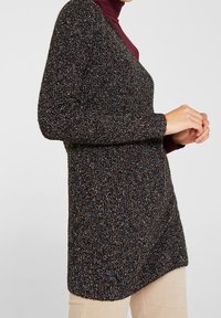 Korte mouwen, donkere gebreide trui met veelkleurige spikkels. Beschikt over een V-hals en een licht asymmetrische zoom. Zachte, gestructureerde stof.
