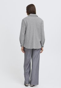 Sivá vlnená košela s golierom, gombíkovými manžetami a voľným strihom, skombinovaná so svetlosivými pruhovanými nohavicami.